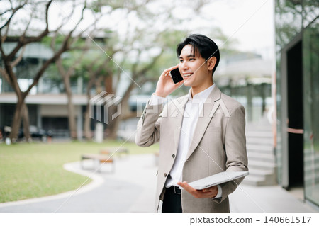 Asian businessman using smartphone outside modern office, mobile business, digital communication, startup growth, online success and professional lifestyle concept. Asian businessman using smartphone outside modern office, mobile business, digital communication, startup growth, online success and professional lifestyle concept. 140661517