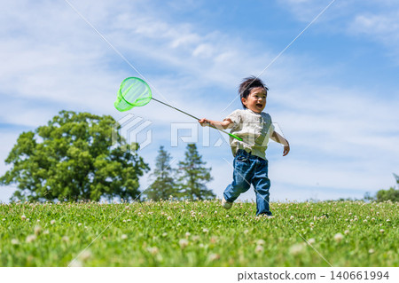 A boy running across a grassy field under a blue sky, carrying a butterfly net. A boy running across a grassy field under a blue sky, carrying a butterfly net. 140661994