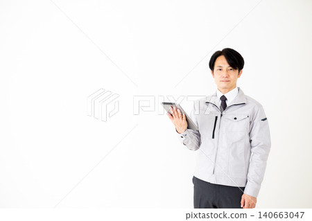 一位身穿灰色工作服的中年商務人士手持平板電腦,背景為白色。 一位身穿灰色工作服的中年商務人士手持平板電腦,背景為白色。 140663047