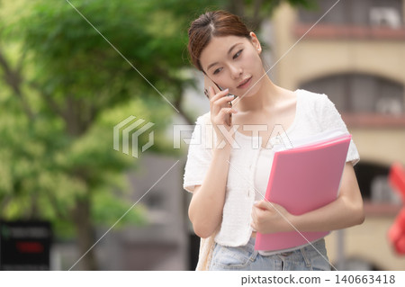 一位年輕女子一邊用智慧型手機通話,一邊陷入沉思。 一位年輕女子一邊用智慧型手機通話,一邊陷入沉思。 140663418