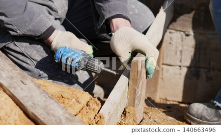 Power Tool Fastening. Handheld Device Driving Screw Into Temporary Concrete Mold Structure. Gloved Hands Operating Cordless Drill To Fasten Formwork During Construction Process Power Tool Fastening. Handheld Device Driving Screw Into Temporary Concrete Mold Structure. Gloved Hands Operating Cordless Drill To Fasten Formwork During Construction Process 140663496