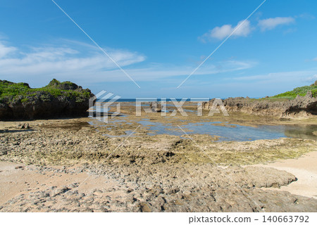 A clear blue sky and a shallow beach with tide pools still remaining. 140663792