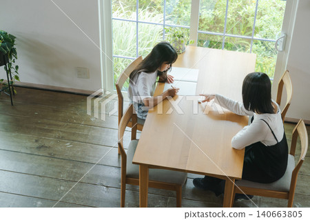 A girl doing her homework and her mother watching over her. A girl doing her homework and her mother watching over her. 140663805