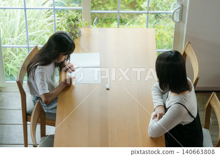 一個女孩在做作業，她的母親在一旁看著。 140663808
