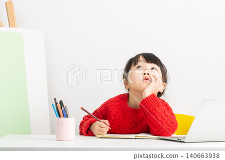 A bright and focused Asian girl is doing her homework at her desk, her expression one of deep thought. A bright and focused Asian girl is doing her homework at her desk, her expression one of deep thought. 140663938
