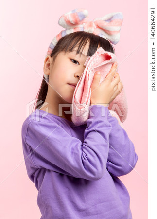 A studio shot of a young Asian girl with long dark hair and a striped headband, wearing a purple sweatshirt, playfully holding a pink hand towel in front of her face, partially obscuring it, against a A studio shot of a young Asian girl with long dark hair and a striped headband, wearing a purple sweatshirt, playfully holding a pink hand towel in front of her face, partially obscuring it, against a 140664291