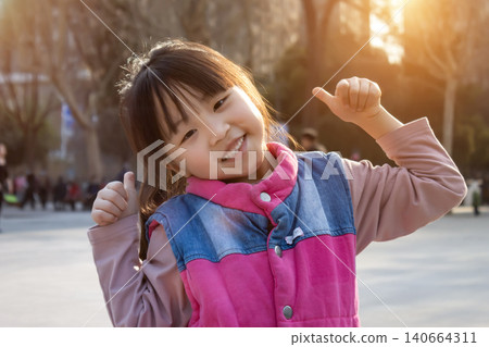 a happy and cute little girl gives a thumbs-up pose on a community road. a happy and cute little girl gives a thumbs-up pose on a community road. 140664311