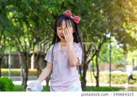 A young girl covers one eye and shouts playfully with a wide open mouth in an outdoor park. A young girl covers one eye and shouts playfully with a wide open mouth in an outdoor park. 140664325