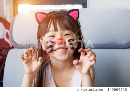 Happy little girl with cat face paint smiling and making claw gestures indoors. Happy little girl with cat face paint smiling and making claw gestures indoors. 140664326