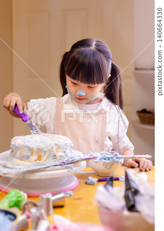Concentrated little girl painting a DIY cake with colorful cream during a baking craft class. Concentrated little girl painting a DIY cake with colorful cream during a baking craft class. 140664330