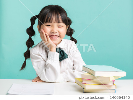 A confident young student sitting at a desk next to a stack of textbooks with her arms folded and a big smile. A confident young student sitting at a desk next to a stack of textbooks with her arms folded and a big smile. 140664340