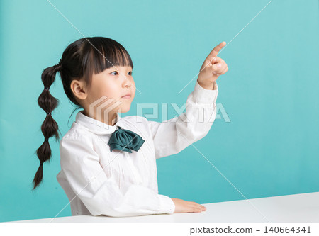 Thoughtful Asian schoolgirl pointing finger thinking isolated on blue background, education idea concept 140664341