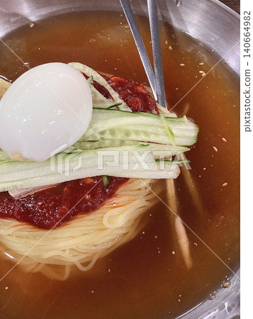 Chilled, chewy naengmyeon noodles in tangy broth paired with juicy, savory mandu dumplings, offering a perfect balance of refreshing coolness and hearty comfort in every delicious Korean bite. Chilled, chewy naengmyeon noodles in tangy broth paired with juicy, savory mandu dumplings, offering a perfect balance of refreshing coolness and hearty comfort in every delicious Korean bite. 140664982