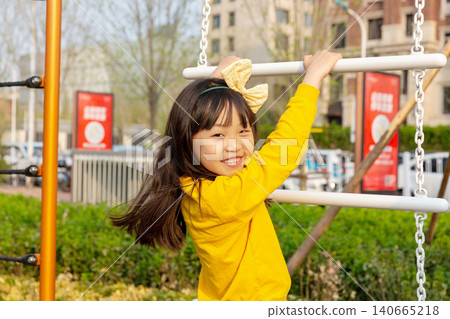 Joyful little girl smiles excitedly while playing inside a rope climbing net at an outdoor playground. Joyful little girl smiles excitedly while playing inside a rope climbing net at an outdoor playground. 140665218