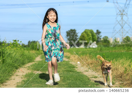 Asian little girl running with dog on grassy path under blue sky, joyful childhood outdoor activity and freedom concept 140665236
