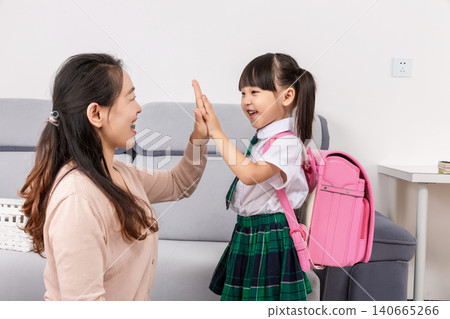 A smiling mother giving a high five to her young daughter in a school uniform to encourage her before school starts. A smiling mother giving a high five to her young daughter in a school uniform to encourage her before school starts. 140665266