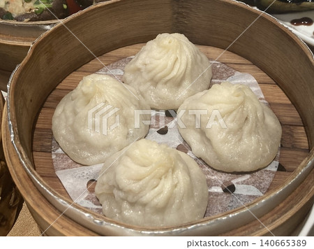 Steamed xiaolongbao dumplings with delicate thin skin, slightly translucent top folds, and savory soup filling inside, highlighting their soft texture and freshly steamed appearance in close-up detail Steamed xiaolongbao dumplings with delicate thin skin, slightly translucent top folds, and savory soup filling inside, highlighting their soft texture and freshly steamed appearance in close-up detail 140665389