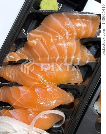 Fresh salmon sushi with bright orange slices placed on top of perfectly shaped rice, garnished with green leaves and radish for a simple, colorful, and appetizing presentation 140665410
