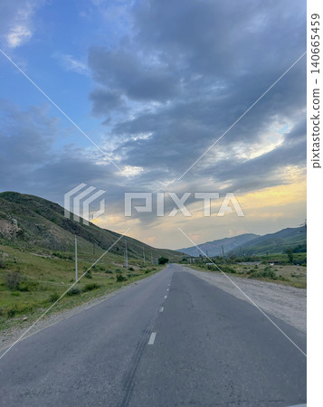 Empty countryside road surrounded by lush green trees and mountain peaks Empty countryside road surrounded by lush green trees and mountain peaks 140665459