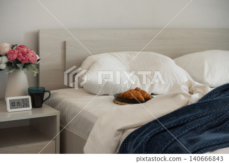 Cozy bedroom breakfast with croissants and coffee beside an unmade bed 140666843