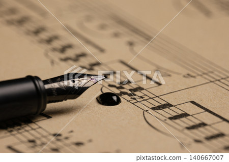 Close-up of a fountain pen nib resting on printed sheet music with a dark ink drop on warm paper Close-up of a fountain pen nib resting on printed sheet music with a dark ink drop on warm paper 140667007