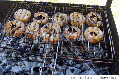 Large stuffed field mushrooms cooking on a wire grill over hot charcoal embers during an outdoor barbecue, displaying a juicy texture and golden-brown char. Large stuffed field mushrooms cooking on a wire grill over hot charcoal embers during an outdoor barbecue, displaying a juicy texture and golden-brown char. 140667104