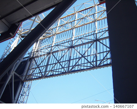 Low-angle shot of a massive metal truss framework and industrial steel support structure of a stadium scoreboard or billboard against a clear blue sky background. Low-angle shot of a massive metal truss framework and industrial steel support structure of a stadium scoreboard or billboard against a clear blue sky background. 140667107