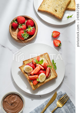 Toasted bread with chocolate cream, strawberries, and banana on a plate on a marble background 140667266