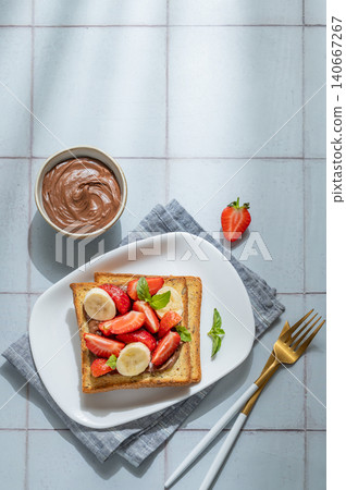 Toasted bread with chocolate cream, strawberries, and banana on a plate on a tile background Toasted bread with chocolate cream, strawberries, and banana on a plate on a tile background 140667267