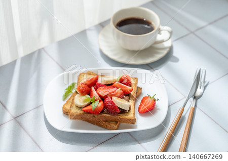 Toasted bread with chocolate cream, strawberries, and banana on a plate on a tile  background 140667269