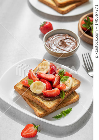 Toasted bread with chocolate cream, strawberries, and banana on a plate on a concrete background Toasted bread with chocolate cream, strawberries, and banana on a plate on a concrete background 140667271