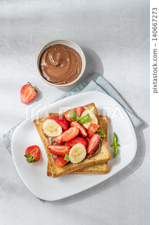 Toasted bread with chocolate cream, strawberries, and banana on a plate on a concrete background Toasted bread with chocolate cream, strawberries, and banana on a plate on a concrete background 140667273