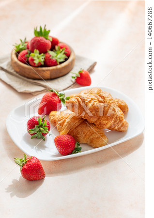 Freshly baked croissants on a plate with strawberries on a bright textured background. Freshly baked croissants on a plate with strawberries on a bright textured background. 140667288