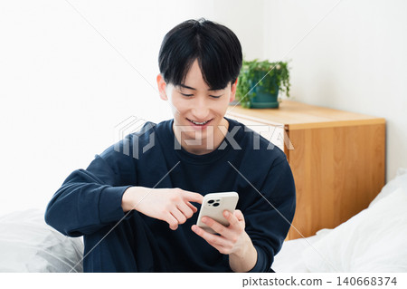 年輕人在床上觀看智能手機 140668374