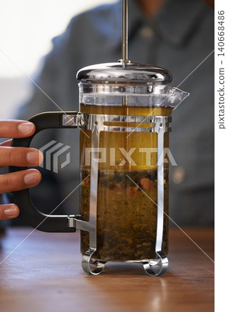 Closeup, person and hands with tea plunger for brewing, heathy and fresh beverage start morning. Cafe, table and prepare for customers on breakfast to taste, drink and enjoy for beautiful day. Closeup, person and hands with tea plunger for brewing, heathy and fresh beverage start morning. Cafe, table and prepare for customers on breakfast to taste, drink and enjoy for beautiful day. 140668486