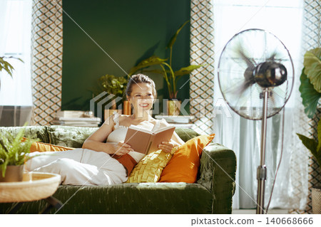Woman Reading Comfortably by Fan in Sunlit Home Woman Reading Comfortably by Fan in Sunlit Home 140668666