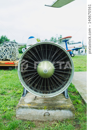 Jet engine sits on a concrete pad at an outdoor aviation display in the daytime with green grass and other aircraft in the background 140670561