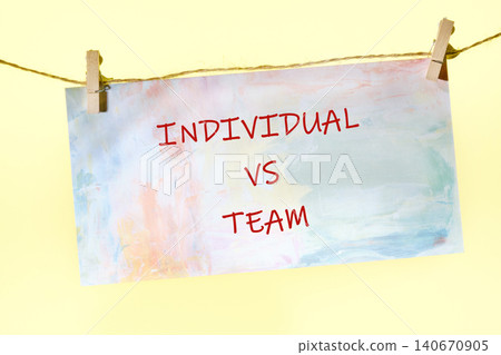 A sign is hanging on a string. The sign has the words individual vs team written in bold letters. The background is light and colorful A sign is hanging on a string. The sign has the words individual vs team written in bold letters. The background is light and colorful 140670905