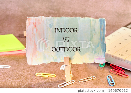 A sign with the words indoor vs outdoor is displayed on a table. The table has colorful sticky notes, paper clips, and a calculator nearby A sign with the words indoor vs outdoor is displayed on a table. The table has colorful sticky notes, paper clips, and a calculator nearby 140670912