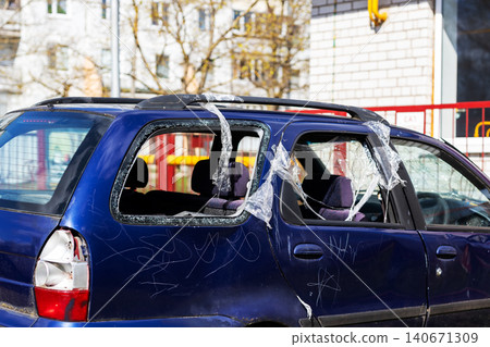 Damaged blue hatchback car with shattered rear windows parked on city street Damaged blue hatchback car with shattered rear windows parked on city street 140671309