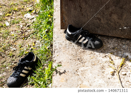 Worn black athletic shoe left beside concrete step on sunlit ground Worn black athletic shoe left beside concrete step on sunlit ground 140671311