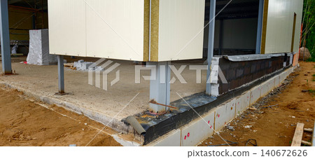 Construction site showing the foundation and support structure of a building with metal columns and concrete base on a sandy ground 140672626