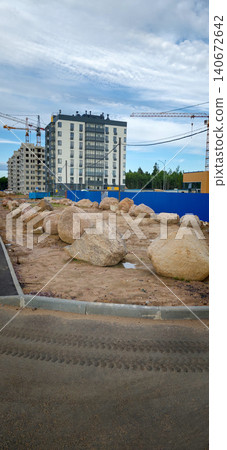 Large boulders arranged on a construction site with residential buildings and cranes in the background under a cloudy sky in an urban environment Large boulders arranged on a construction site with residential buildings and cranes in the background under a cloudy sky in an urban environment 140672642
