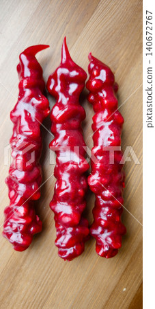 Three elongated red oriental sweets arranged on a wooden surface, showcasing a glossy texture and unique twisted shape, ideal for traditional celebrations and cultural events 140672767