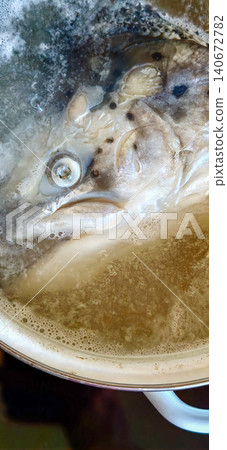 Whole fish boiling in a pot of water, with bubbles rising and a clear view of the fish's head and eye, showcasing cooking preparation in a kitchen setting Whole fish boiling in a pot of water, with bubbles rising and a clear view of the fish's head and eye, showcasing cooking preparation in a kitchen setting 140672782
