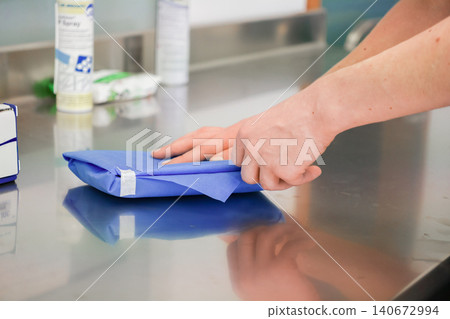 Medical professional hands wrapping surgical instruments in a blue sterilization drape on a clean stainless steel table to ensure hospital safety and equipment hygiene protocols 140672994