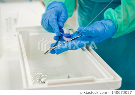 A dedicated medical professional carefully cleans surgical instruments with a small brush and a basin of water to ensure proper sterilization protocols for patient safety today A dedicated medical professional carefully cleans surgical instruments with a small brush and a basin of water to ensure proper sterilization protocols for patient safety today 140673037
