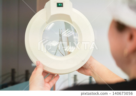 Medical professional examines stainless steel dental surgical forceps through a circular magnifying glass to ensure high quality precision and hygiene in a clinical lab environment Medical professional examines stainless steel dental surgical forceps through a circular magnifying glass to ensure high quality precision and hygiene in a clinical lab environment 140673056
