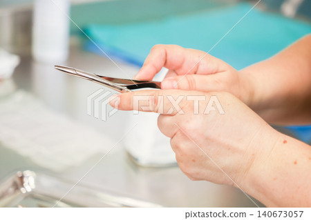 A medical professional holds a stainless steel surgical hemostat tool at a sterile clinic table, representing clinical precision and expertise during a complex surgical procedure 140673057
