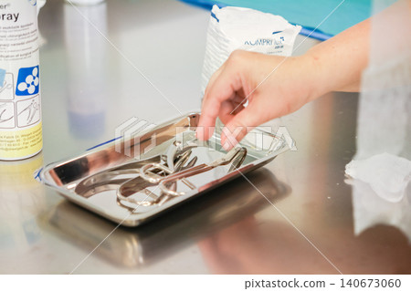 Medical professional hand reaches for surgical instruments on a metal tray in a clinic room, illustrating precise preparation for clinical procedures and sterile healthcare standards Medical professional hand reaches for surgical instruments on a metal tray in a clinic room, illustrating precise preparation for clinical procedures and sterile healthcare standards 140673060